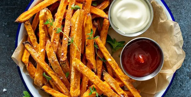 Plate of sweet potato fries cooked in the air fryer with bowls of ketchup and mayonnaise