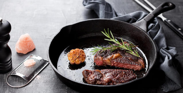 Cast-iron pan with sirloin steak, garlic and rosemary with pink rock salt