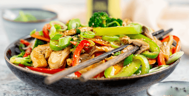 Chicken and vegetable stir-fry with chopsticks in flat bowl