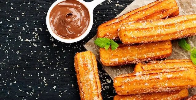 Plate of air-fried churros with chocolate dip on black background